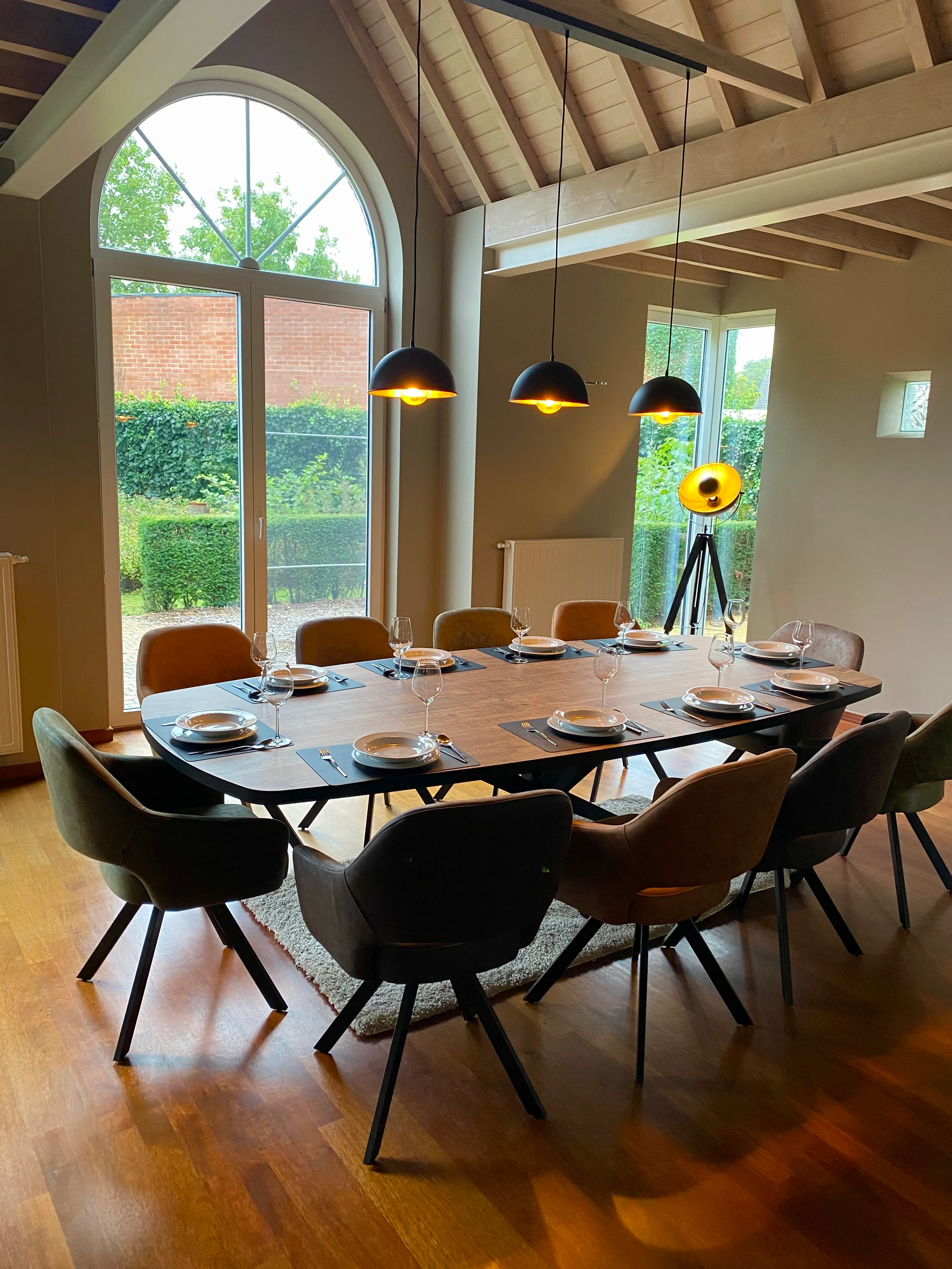De eetkamer met een gedekte tafel voor tien, met een hoog boograam dat op de tuin uitkijkt
