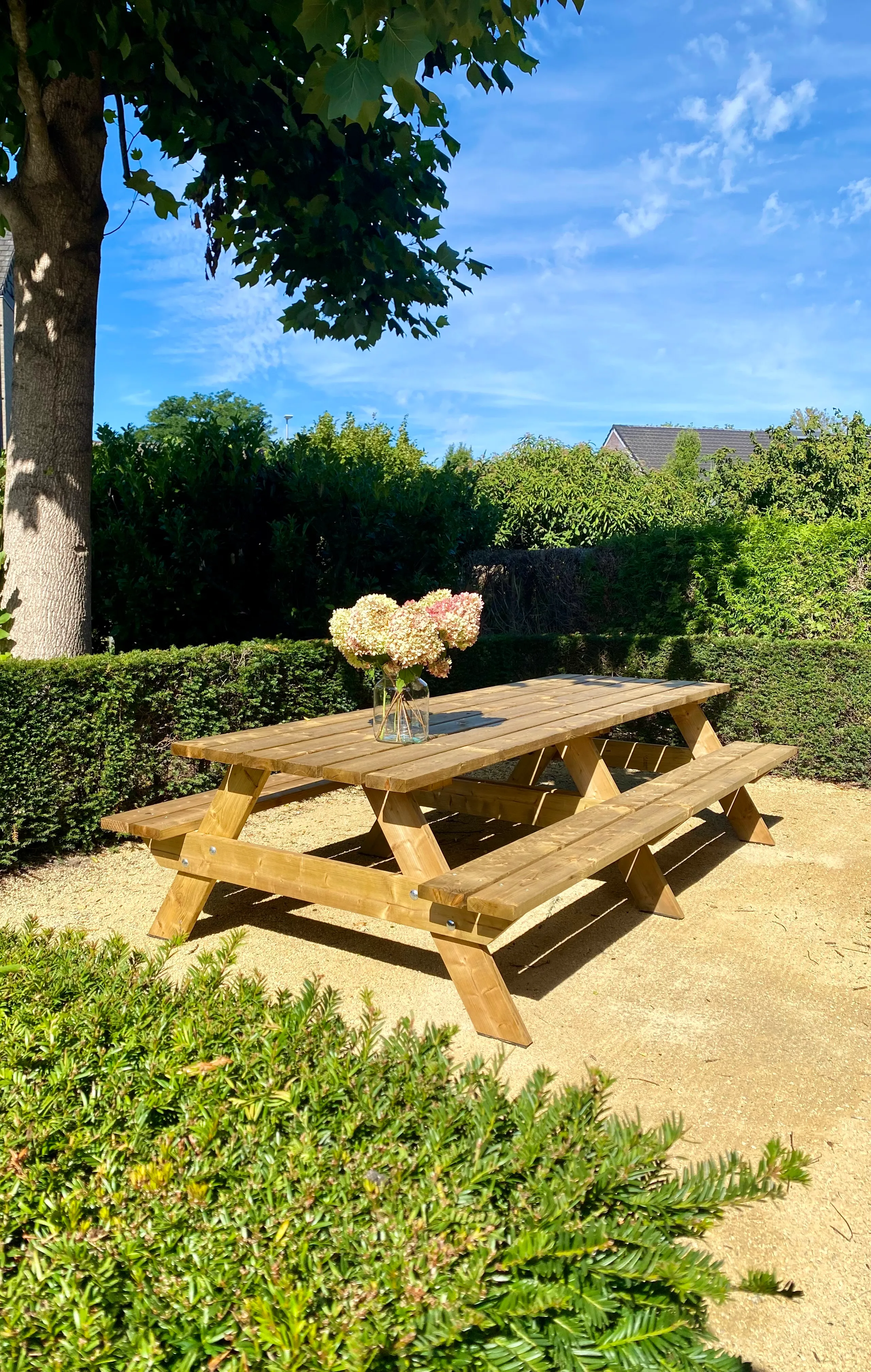 Houten picknicktafel in de schaduw van een boom, met een vaas hortensia's erop