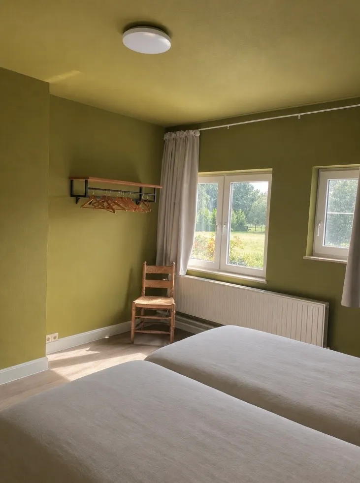 Slaapkamer met twee ramen die uitkijken op het veld achter het huis