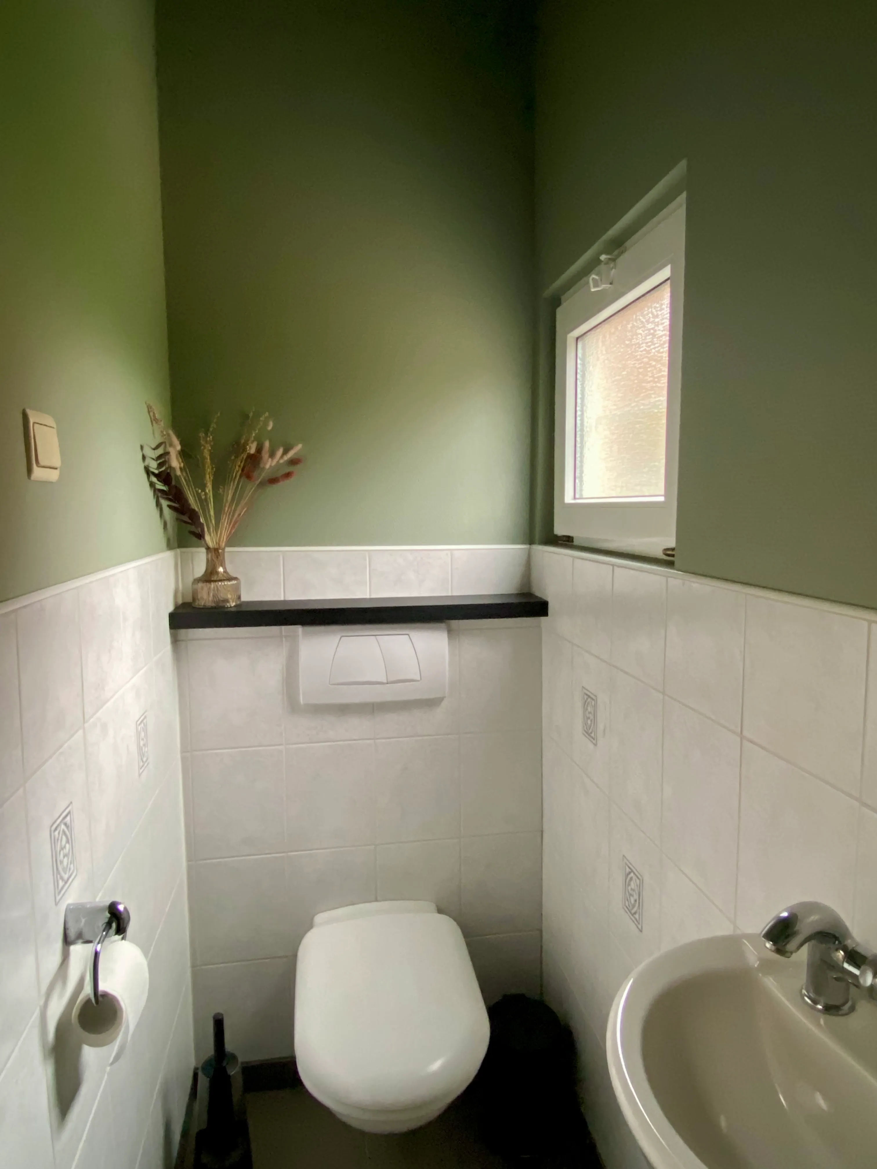 Apart toilet met groene muren, witte tegels en een fonteintje